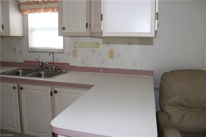 Kitchen featuring wallpapered walls, light countertops, a sink, and white cabinets