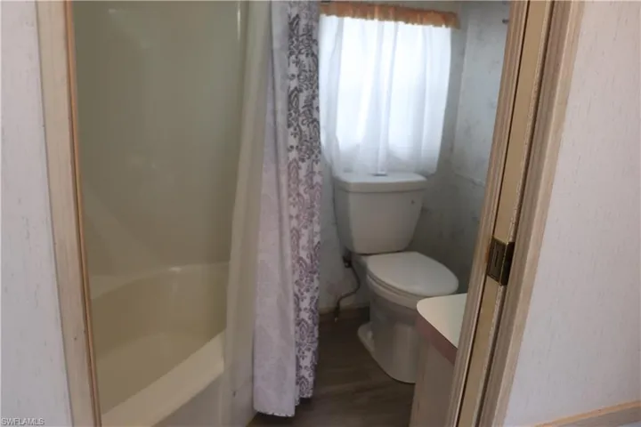 Full bath featuring a bathing tub, toilet, wood finished floors, vanity, and curtained shower