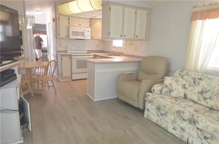 Kitchen with light countertops, light wood-type flooring, white appliances, backsplash, and a peninsula