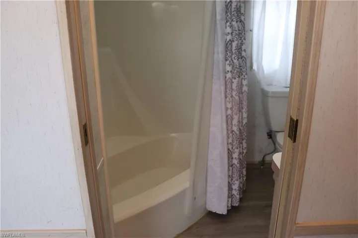 Full bath with toilet, a bathtub, a shower with shower curtain, and wood finished floors
