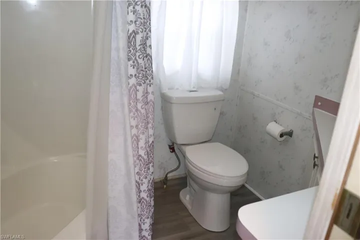 Full bath featuring a shower with curtain, wallpapered walls, toilet, and wood finished floors