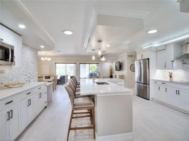 Bright kitchen featuring white shaker cabinetry, stainless steel appliances, quartz countertops, and a large central island with seating