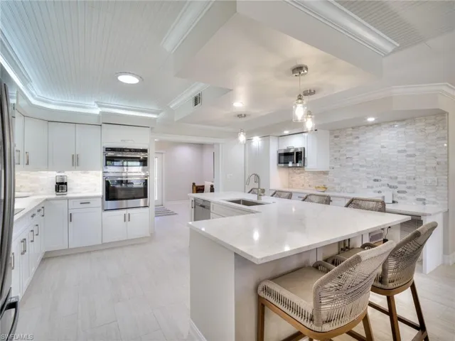 Bright kitchen featuring a large central island with seating, white shaker cabinetry, stainless steel double ovens, and a natural stone mosaic tile backsplash