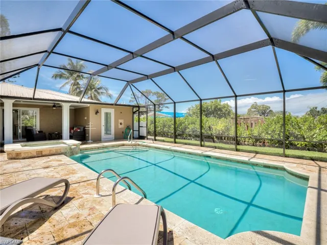 Screened pool enclosure featuring a rectangular pool with integrated spa, stone coping, and a textured patio surround