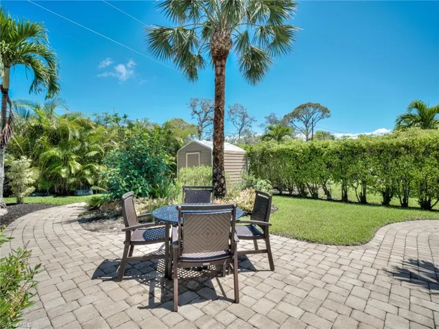 Paver patio area with a central palm tree, surrounded by lush tropical landscaping and a manicured lawn