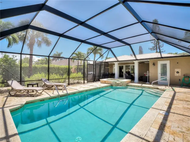 Screened-in outdoor living space featuring an in-ground swimming pool with integrated spa and stone paver surround