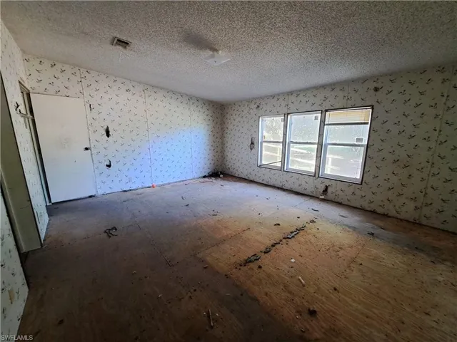 Unfurnished room featuring a textured ceiling and wallpapered walls