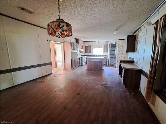 Kitchen featuring dark wood finished floors, a textured ceiling, white range, a center island, and wallpapered walls