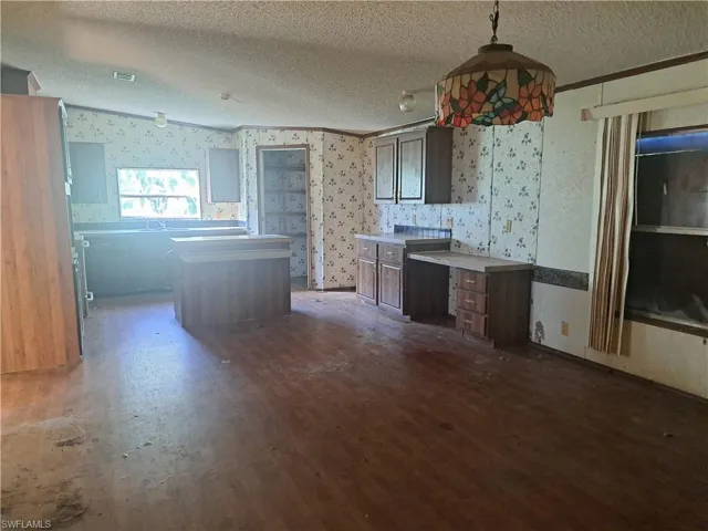 Kitchen with a textured ceiling, a center island, hanging light fixtures, wallpapered walls, and dark wood-style flooring
