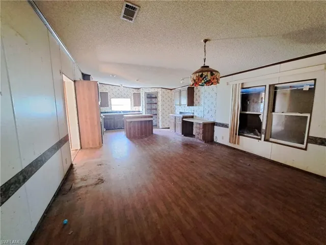 Unfurnished living room featuring ornamental molding, a textured ceiling, dark wood finished floors, and wallpapered walls