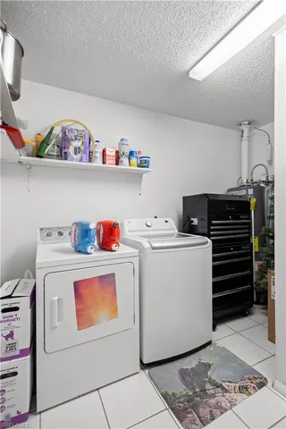 Laundry area with light tile patterned floors, separate washer and dryer, a textured ceiling, and water heater