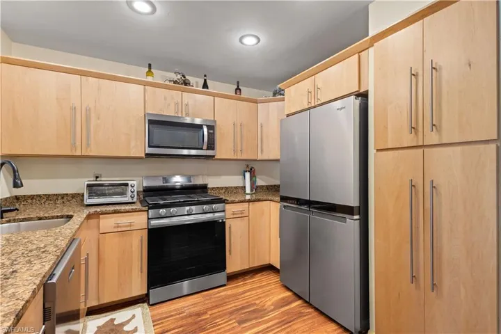 Kitchen with light brown cabinetry, dark stone countertops, appliances with stainless steel finishes, and light wood-style floors