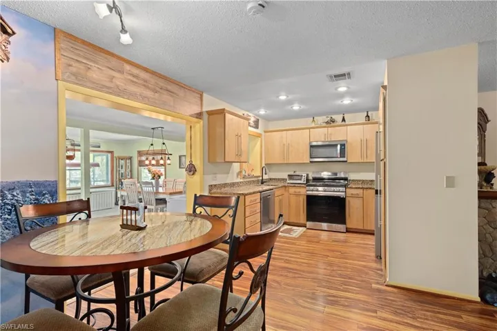 Kitchen with light brown cabinets, stainless steel appliances, light wood-style flooring, a textured ceiling, and light stone countertops