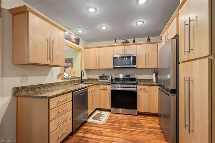 Kitchen with dark stone counters, stainless steel appliances, light brown cabinets, light wood-style floors, and recessed lighting