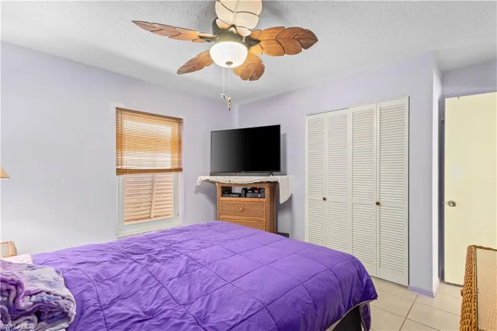 Bedroom with a textured ceiling, light tile patterned floors, a closet, and ceiling fan