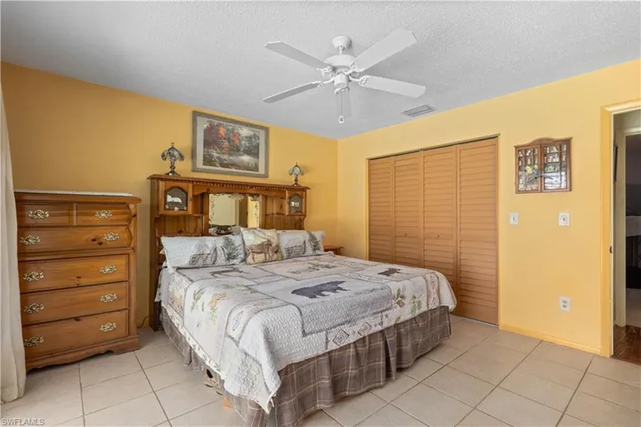 Bedroom featuring a textured ceiling, light tile patterned floors, a closet, and a ceiling fan