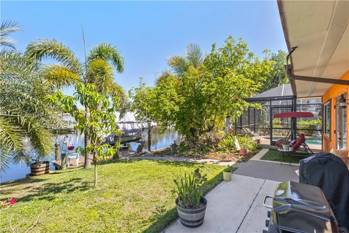 View of green lawn with a sunroom, a water view, glass enclosure, a boat dock, and boat lift