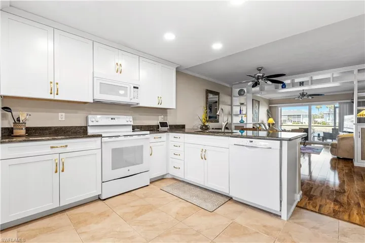 Kitchen with a sink, white appliances, a peninsula, crown molding, and white cabinetry