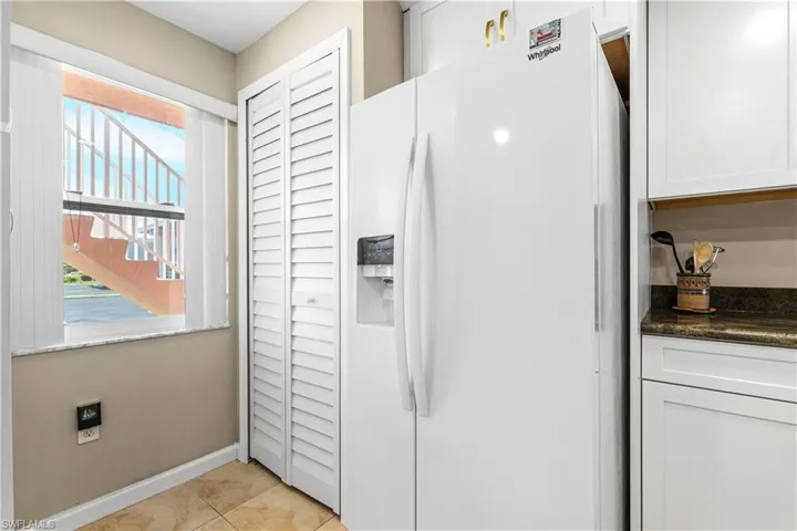 Kitchen featuring light tile patterned floors, white cabinets, baseboards, dark countertops, and white refrigerator