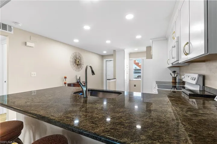 Kitchen featuring white microwave, visible vents, a sink, range with electric stovetop, and a breakfast bar island