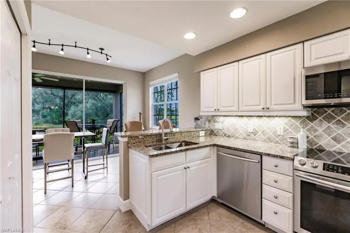 Kitchen with appliances with stainless steel finishes, white cabinets, light stone countertops, a peninsula, and recessed lighting