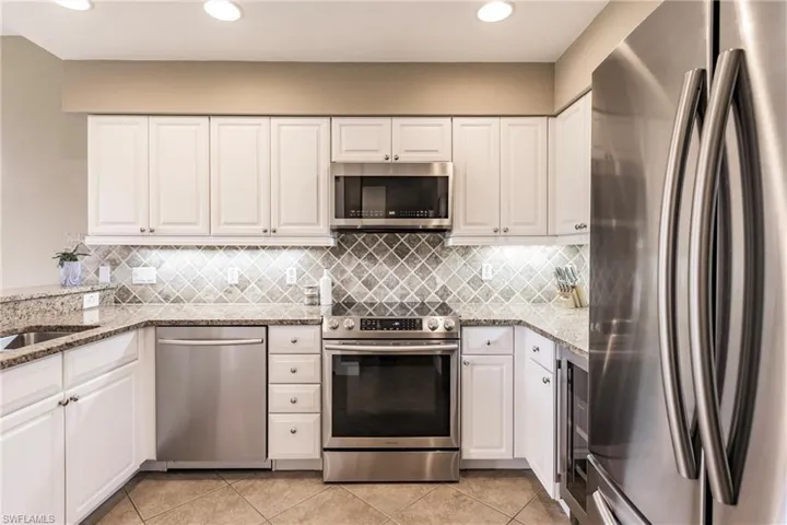 Kitchen featuring stainless steel appliances, white cabinetry, light stone counters, light tile patterned flooring, and recessed lighting