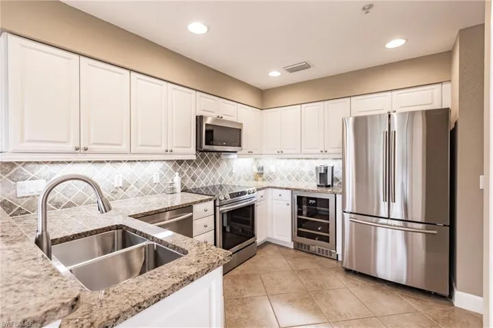 Kitchen with stainless steel appliances, white cabinets, light stone countertops, wine cooler, and light tile patterned floors