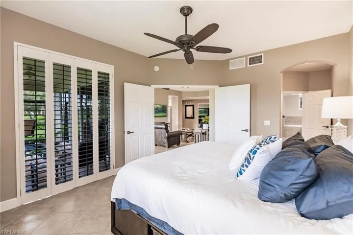 Bedroom featuring access to exterior, ensuite bathroom, light tile patterned floors, a ceiling fan, and arched walkways