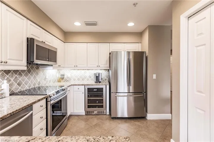 Kitchen featuring stainless steel appliances, wine cooler, white cabinets, light stone countertops, and light tile patterned floors