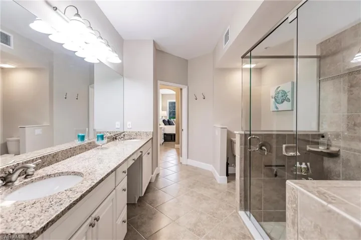 Ensuite bathroom with double vanity, a stall shower, and light tile patterned floors