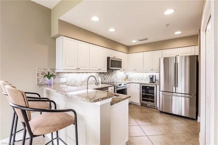 Kitchen featuring a peninsula, stainless steel appliances, light stone counters, white cabinets, and wine cooler