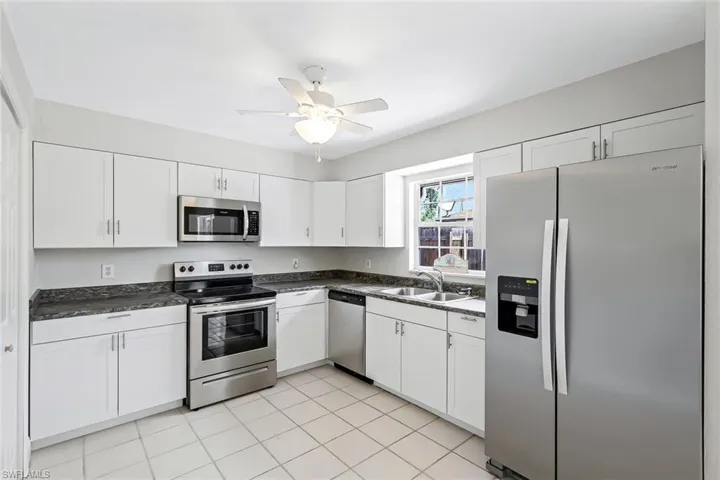 Kitchen featuring stainless steel appliances, dark countertops, white cabinetry, and a ceiling fan