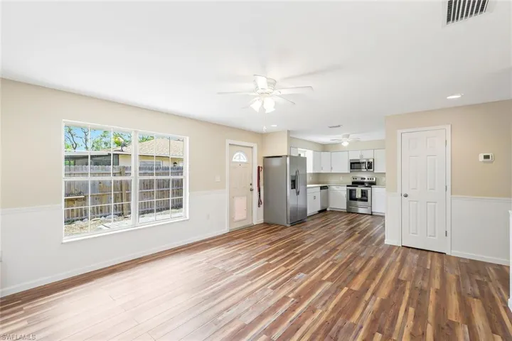 Unfurnished living room featuring ceiling fan, wood finished floors, and wainscoting