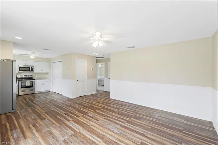 Unfurnished living room with a ceiling fan, dark wood-style floors, and wainscoting