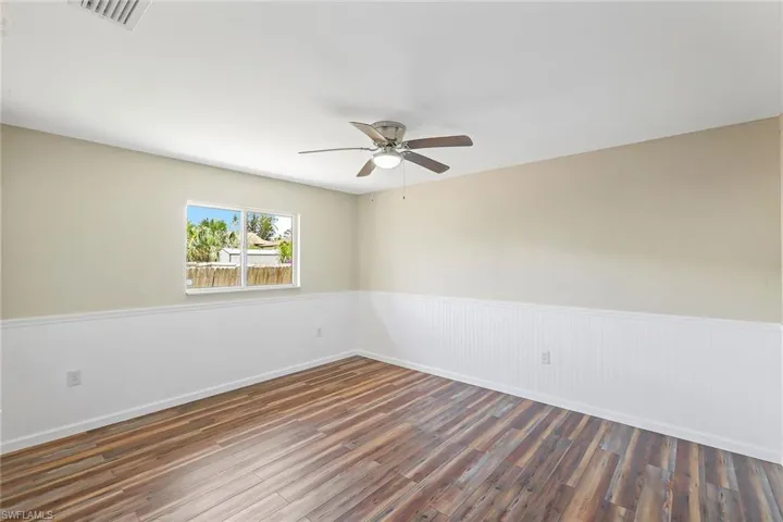 Unfurnished room featuring a ceiling fan, a wainscoted wall, and wood finished floors