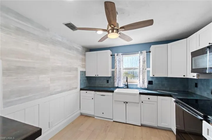 Kitchen with dark countertops, wainscoting, black appliances, white cabinetry, and light wood-style flooring