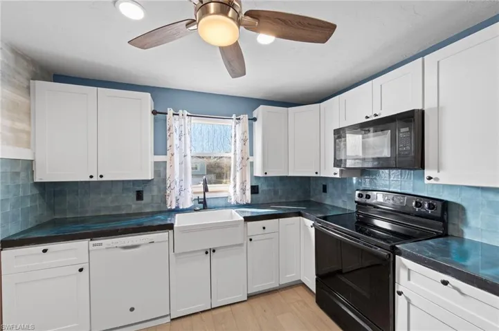 Kitchen with black appliances, light wood-type flooring, white cabinets, and tasteful backsplash