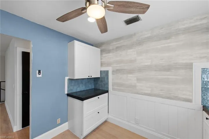 Kitchen featuring white cabinets, a ceiling fan, light wood-style floors, and wainscoting
