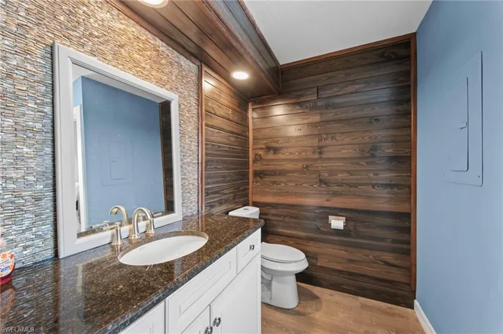 Half bath with vanity, electric panel, light wood finished floors, and wood walls