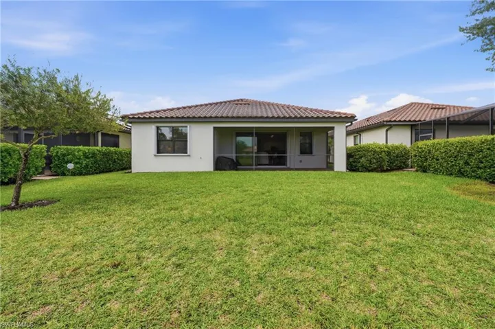 Expansive rear lawn featuring a screened patio entry, stucco exterior, and a tiled roofline