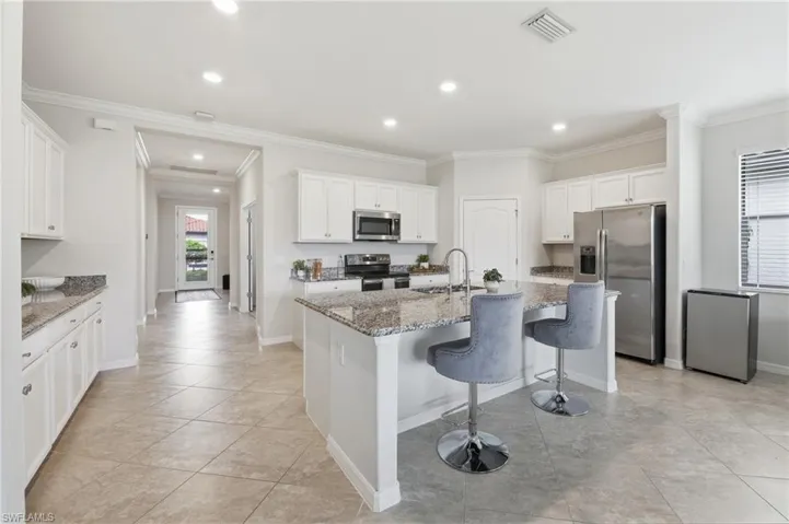 Spacious kitchen featuring an island with stone countertops, white cabinetry, stainless steel appliances, and tile flooring