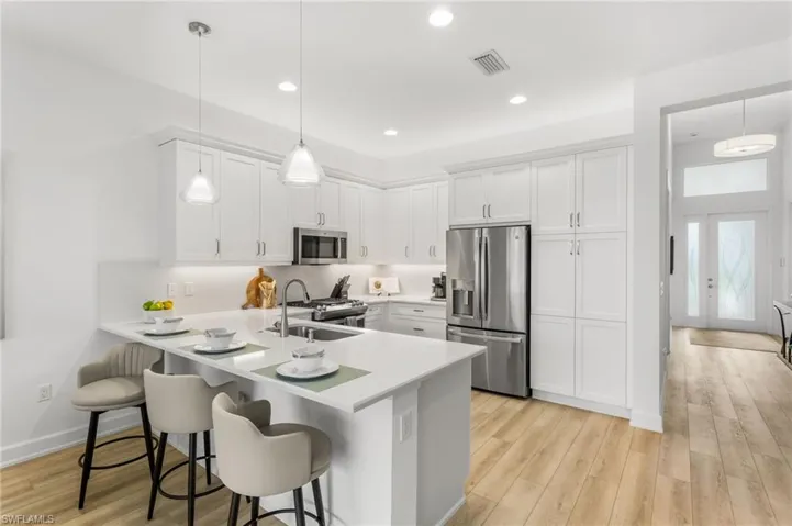 Kitchen with stainless steel appliances, a kitchen bar, light wood-style floors, a peninsula, and white cabinets