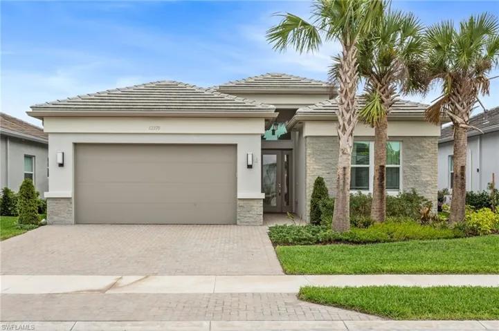 Prairie-style house featuring stone siding, an attached garage, decorative driveway, a front lawn, and stucco siding