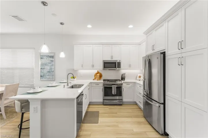 Kitchen featuring a peninsula, stainless steel appliances, a breakfast bar area, white cabinetry, and hanging light fixtures