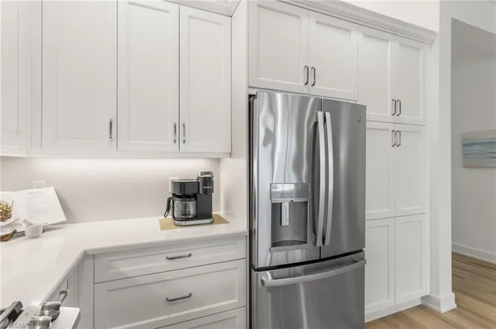 Kitchen with stainless steel refrigerator with ice dispenser, light stone countertops, white cabinets, and light wood finished floors