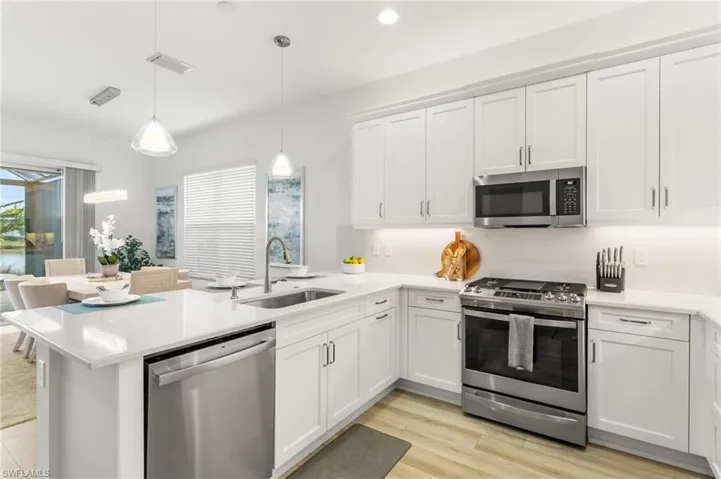 Kitchen with stainless steel appliances, white cabinetry, a peninsula, hanging light fixtures, and light wood-style floors