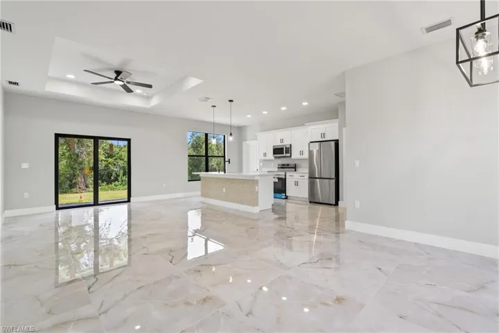 Unfurnished living room featuring ceiling fan, light marble finish floors, recessed lighting, and a tray ceiling