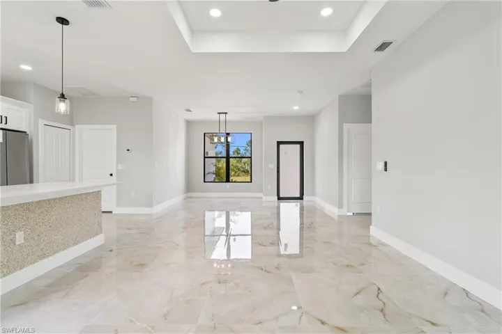 Unfurnished living room with recessed lighting, a raised ceiling, light marble finish flooring, and a chandelier