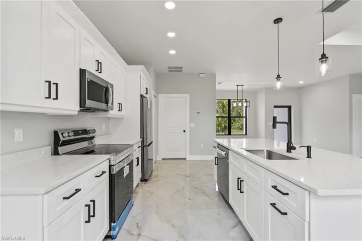 Kitchen with appliances with stainless steel finishes, recessed lighting, light marble finish flooring, white cabinets, and an island with sink