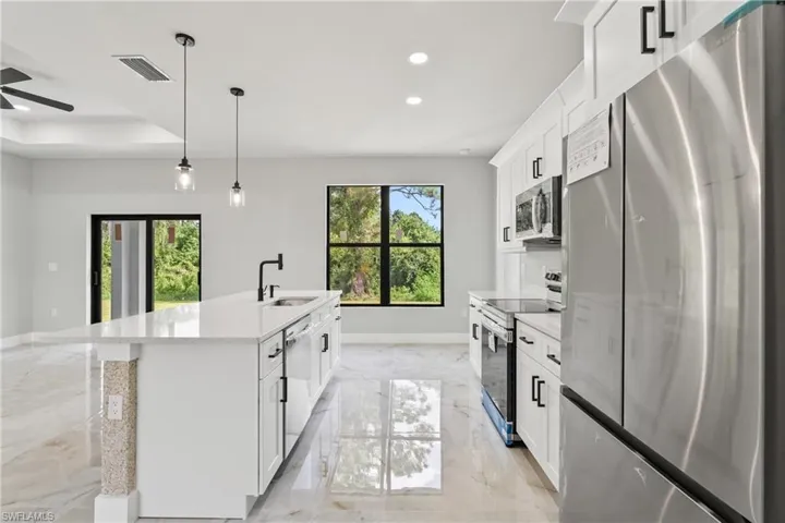 Kitchen with appliances with stainless steel finishes, light marble finish flooring, recessed lighting, white cabinetry, and a kitchen island with sink